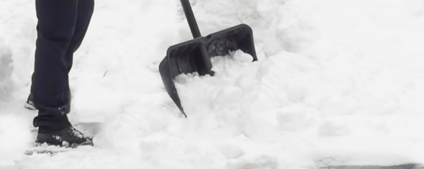 Close-up of a person shoveling heavy snow with a black snow shovel.